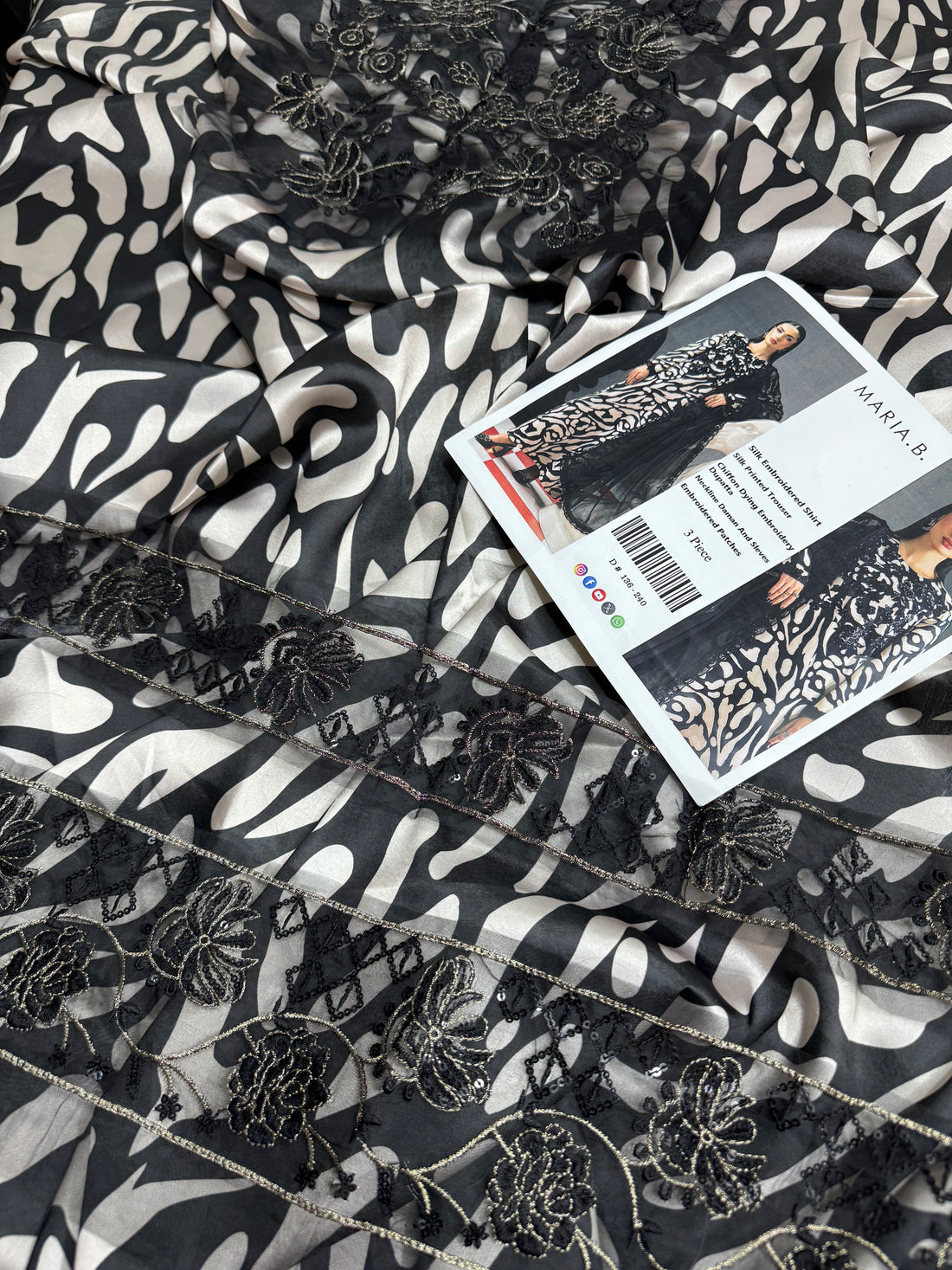 A fashion catalog composite showing a model wearing a long black and beige patterned embroidered dress or kurta set on the left, with text listing the materials and pieces on the center, and a closer view of the garment on the right. The brand name MARIA.