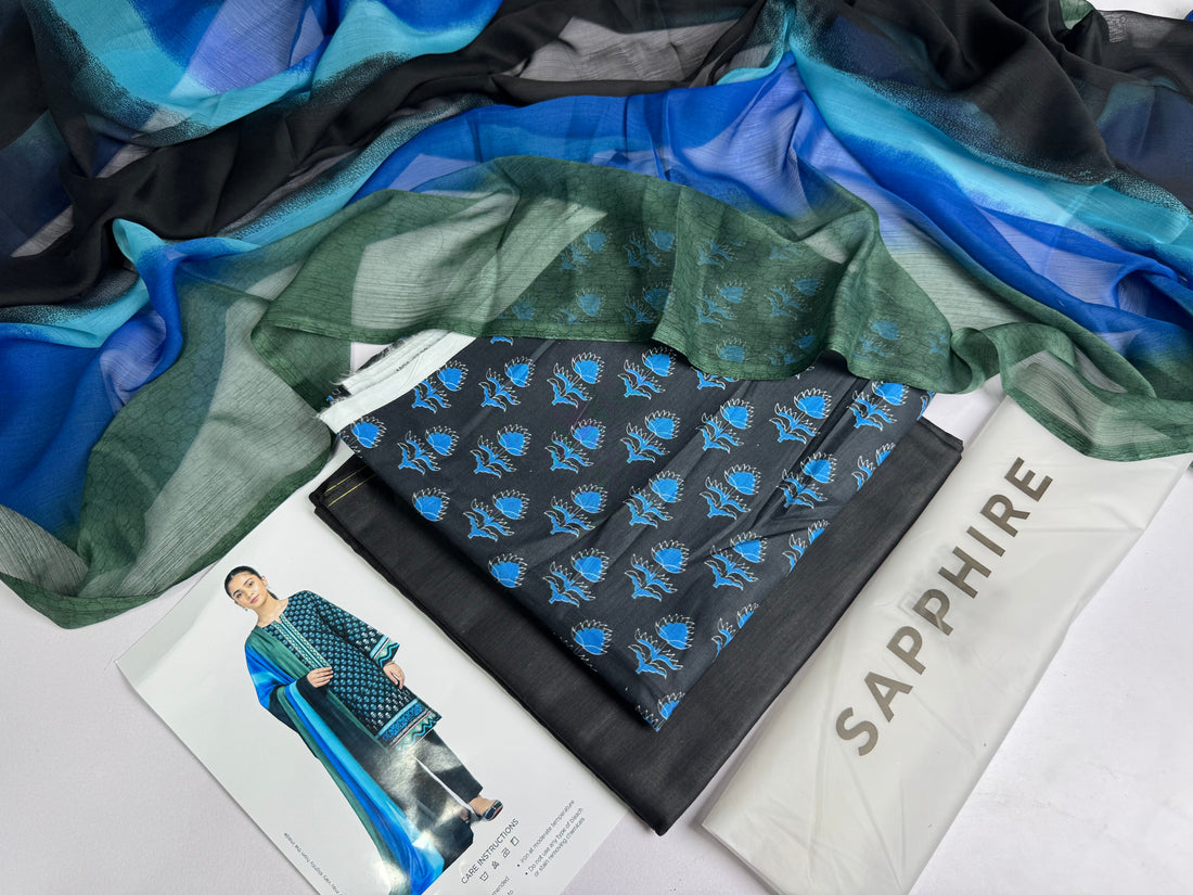 A model wears a three-piece printed lawn suit from Design Stock, featuring a blue and teal kurta with black and gold patterns, a matching printed shirt, and a dupatta. The image is a product information card with text details, a barcode, and care instructions on a white background.