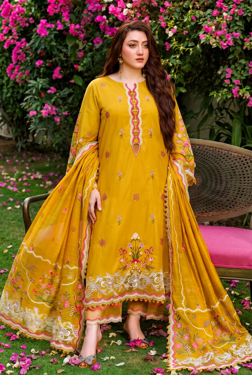 A three-piece women's ethnic wear set from Anabela's Collection, featuring a mustard yellow embroidered shirt, trouser, and pashmina shawl with intricate multicolor embroidery, shown on a model in an outdoor garden setting.