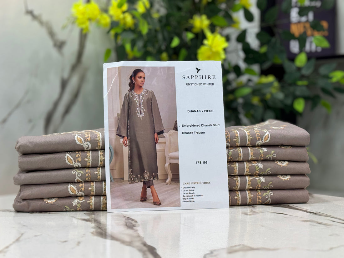 A woman modeling a gray three-piece ethnic wear set, featuring an embroidered Dhanak kurta, shirt, and trouser, presented on a white background with brand text 'SAPPHIRE UNSTICHED WINTER' and product details.