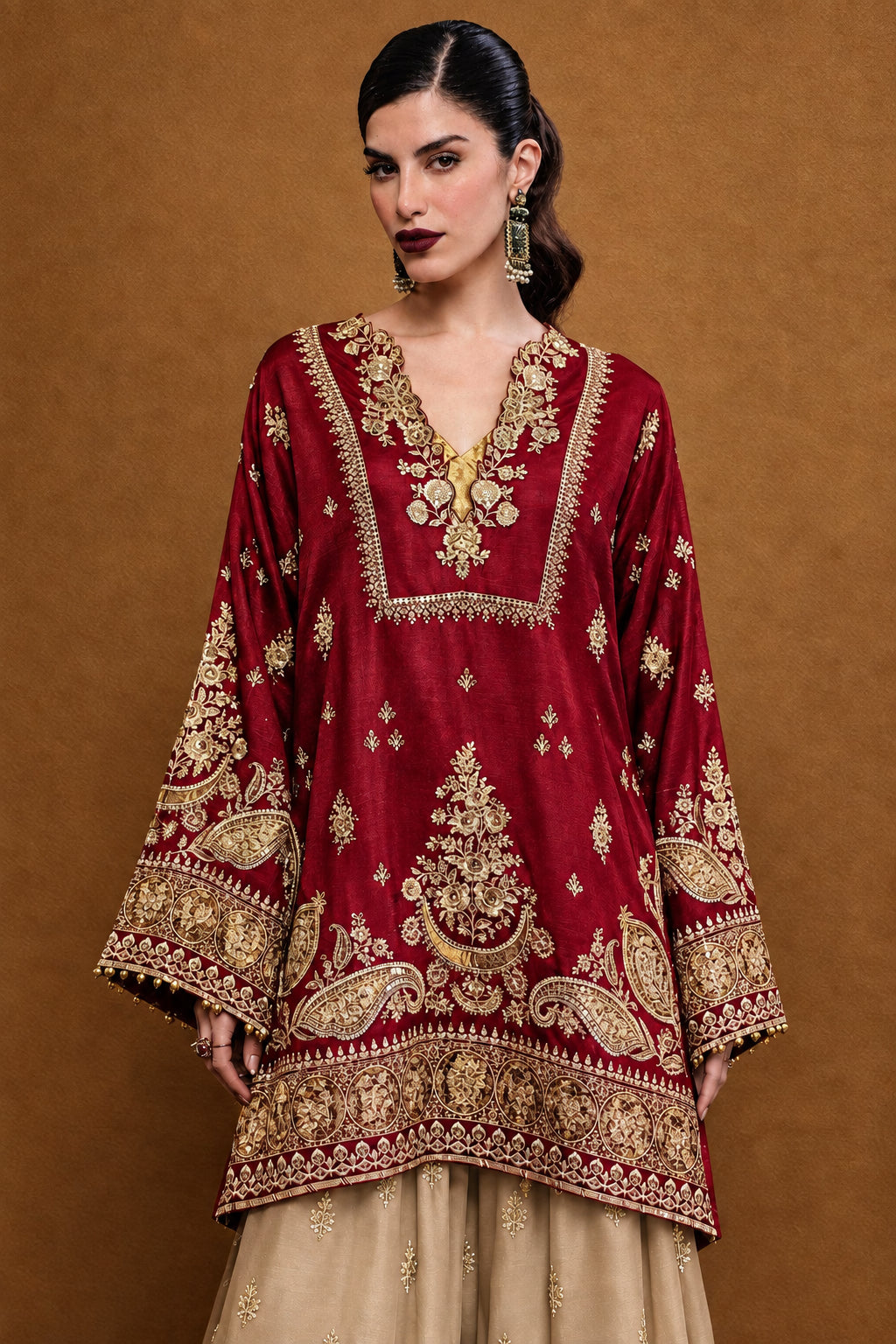 A woman wearing a deep red embroidered kurta with gold and silver metallic detailing, set against a plain brown background.