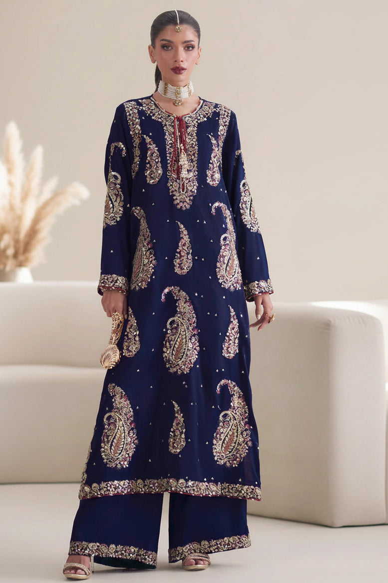 A model wearing a navy blue ethnic two-piece suit with intricate gold and silver paisley embroidery, shown in front and side views on a light beige background. The image includes text overlays describing the product as a 'Silk Embroidered Shirt' and 'Silk Dyed Trouser' with a central white panel labeled 'ETHNIC'.