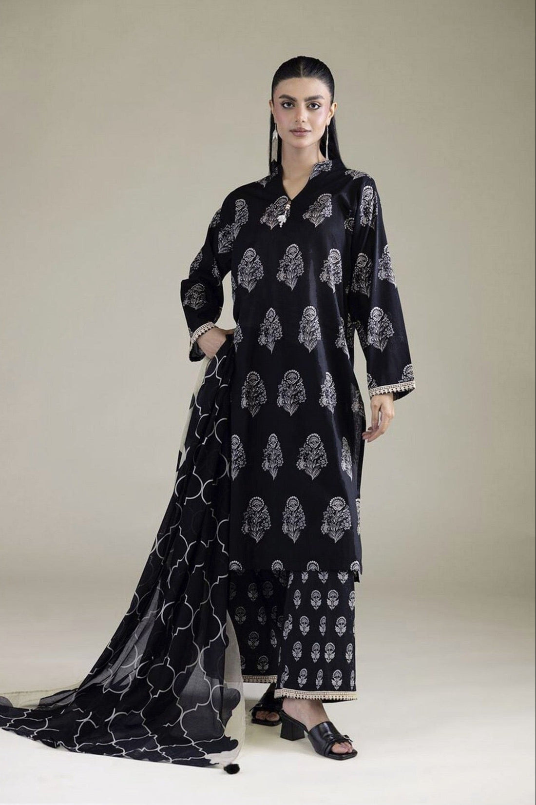 A model wearing a black three-piece suit with white printed motifs, shown against a light beige studio background. The left side of the image features a white panel with product details, care instructions, and a barcode under the brand name KHAADI.