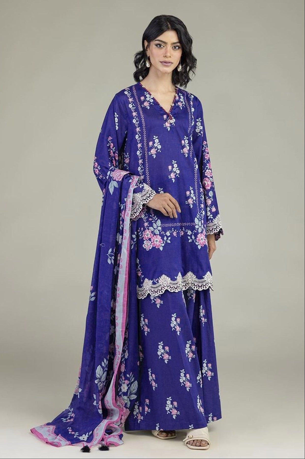 A model wears a purple 3-piece suit set with pink and white floral prints, lace borders, and a matching dupatta. The left side of the image features a white panel with product details, text, and a barcode for Khaadi.