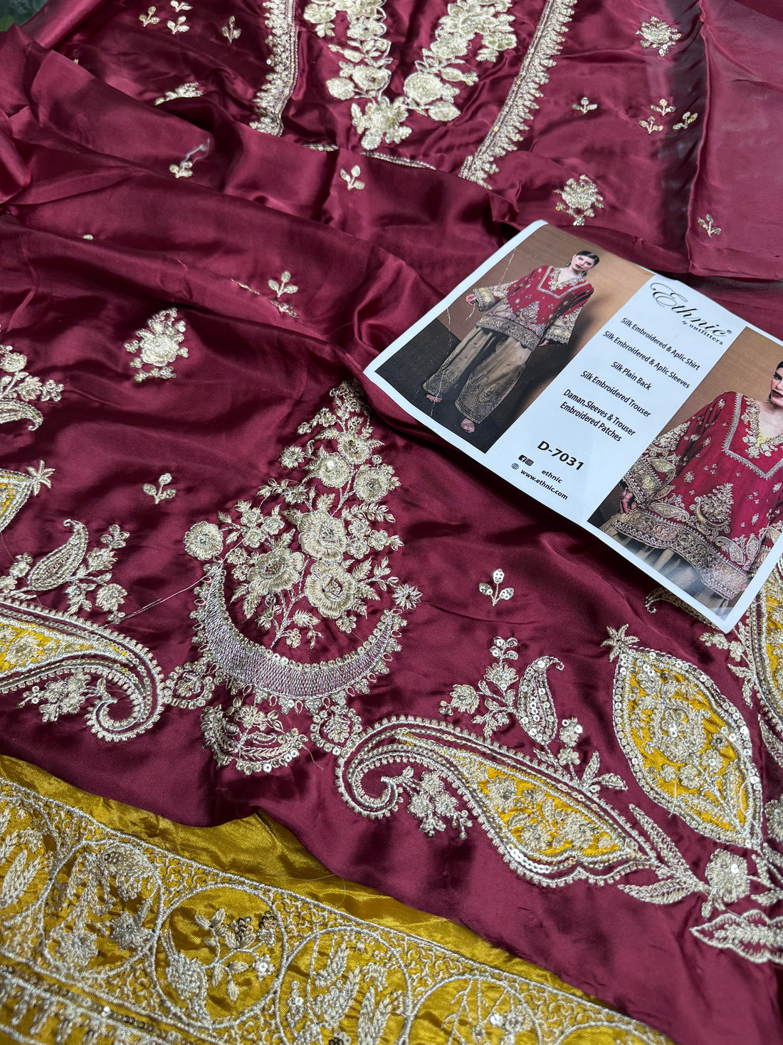 A woman wearing a deep red embroidered kurta with gold and silver metallic detailing, set against a plain brown background.