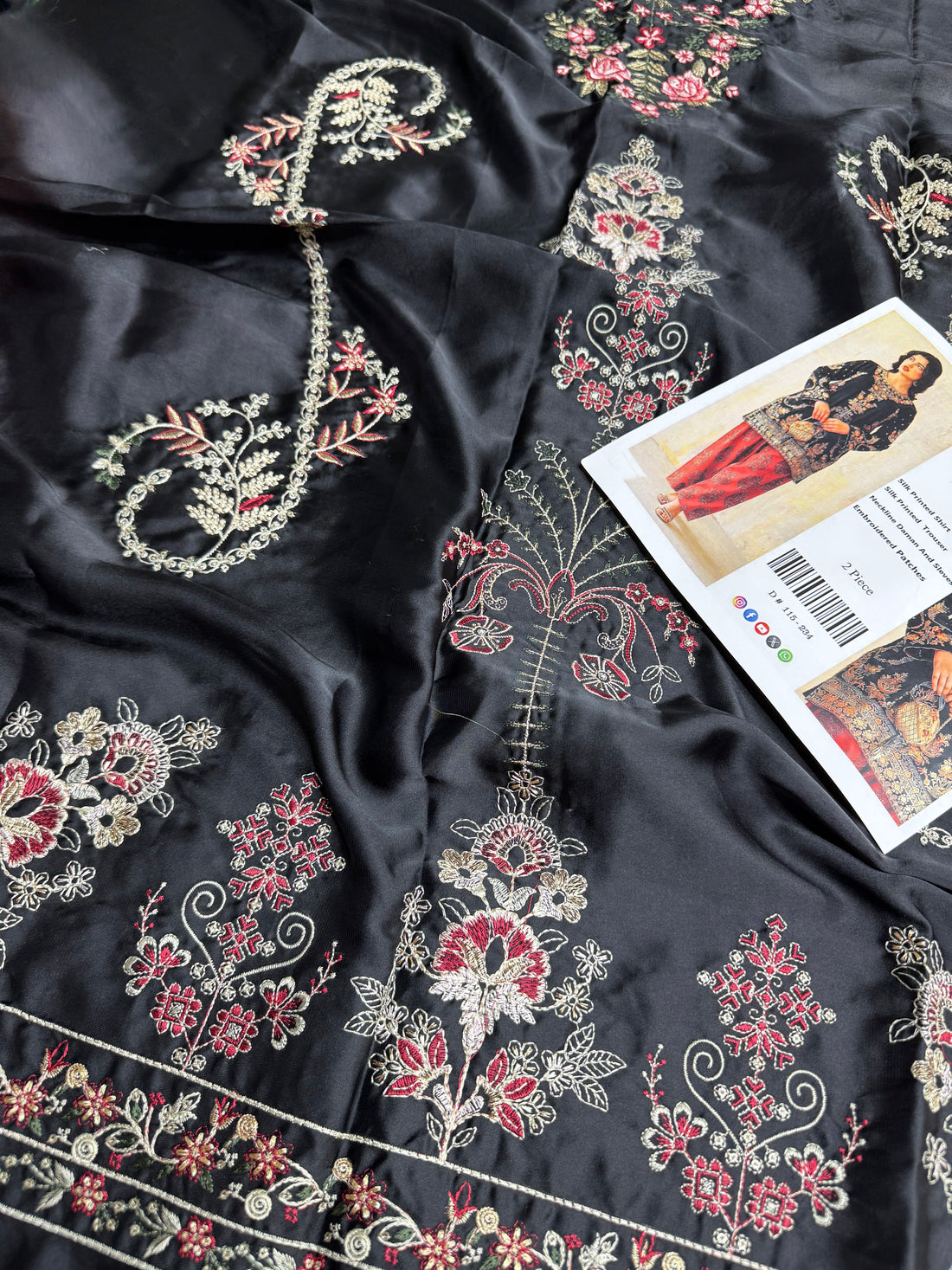 A woman modeling a traditional South Asian outfit featuring a black velvet kurta with intricate gold and silver embroidery, paired with red patola pants, holding a small metallic clutch bag.