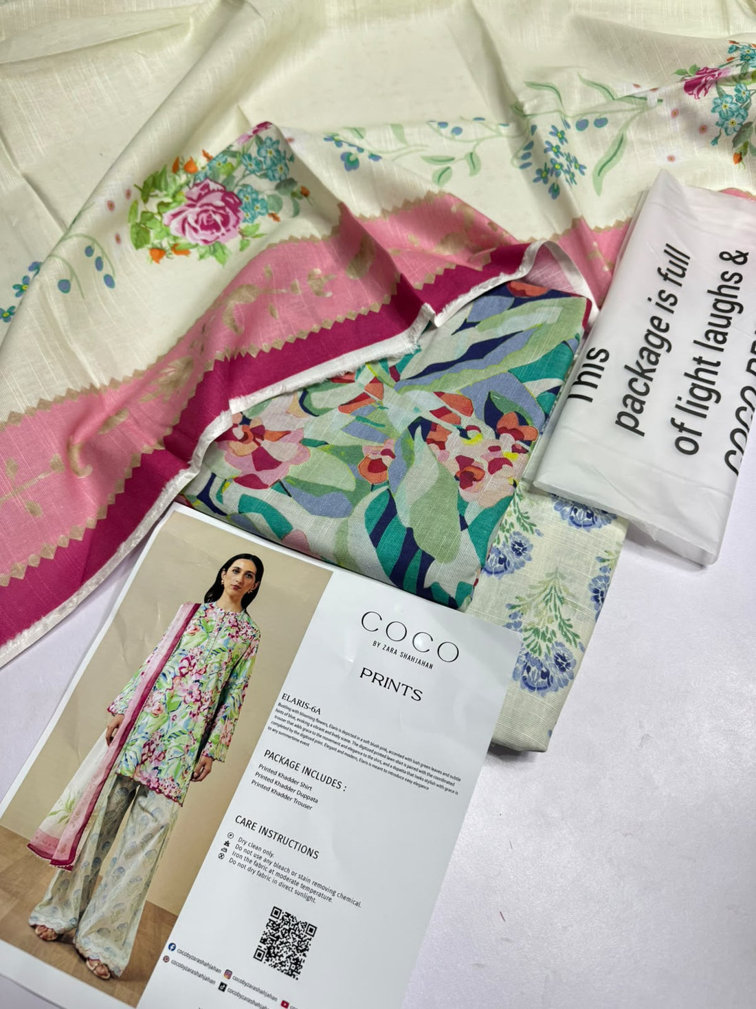 A model wearing a floral printed kurta and matching trousers with a pink border dupatta, shown on the left against a beige studio backdrop. The right side contains brand text reading 'COCO BY ZARA SHAHJAHAN PRINTS', product details for 'ELARIS-6A', package contents, care instructions, and a QR code.