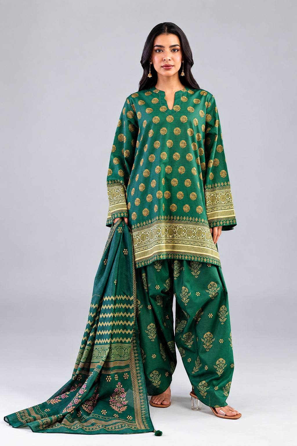 A woman modeling a green three-piece suit set with gold and beige printed motifs, featuring a kurta, bottom fabric, and dupatta, shown on a light gray background with product details and a barcode on the left.