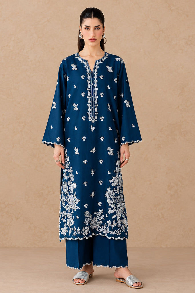 A woman models a navy blue Batik kurta set with white floral block prints and matching pants in a studio setting with rustic clay pots. An inset shows a seated view of the same outfit.
