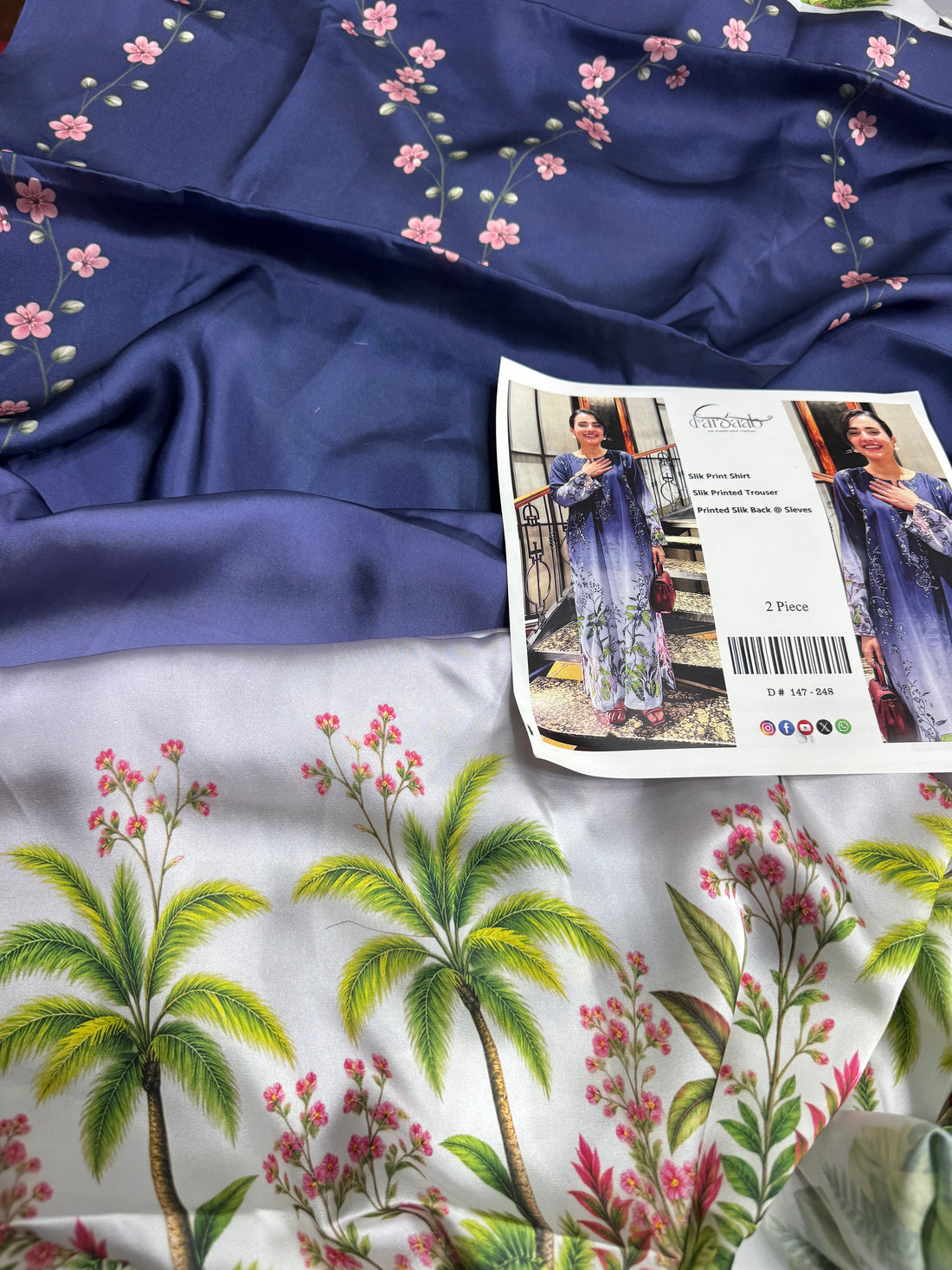 A woman modeling a two-piece silk printed outfit in a split-screen layout, with text details in the center. The outfit is a long-sleeve dress and trouser set in a purple-to-white gradient with floral patterns.