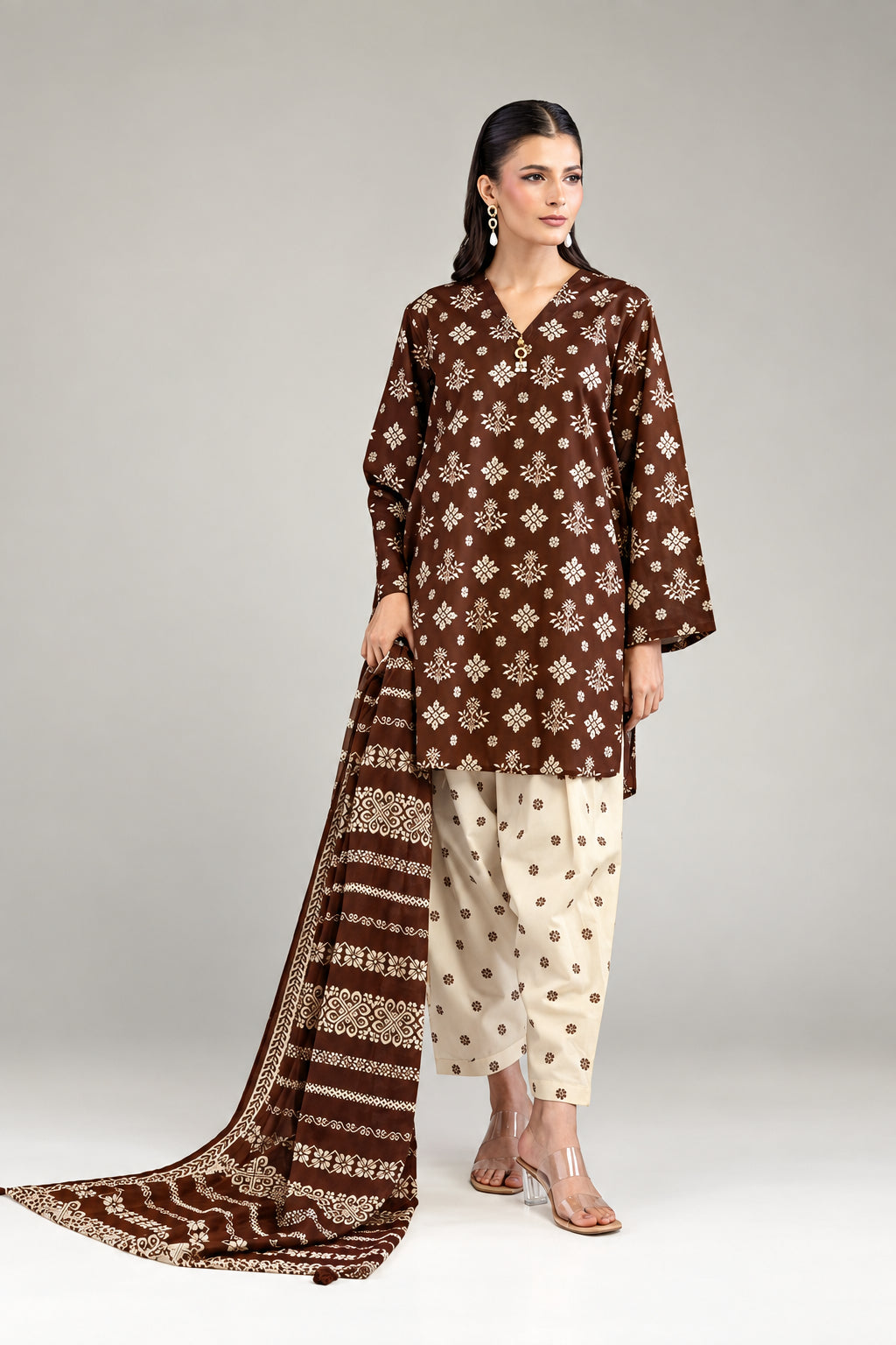 A model wearing a Khaadi 3-piece suit in brown and beige, featuring a printed kurta, trousers, and dupatta, shown next to product specifications and a barcode on a light gray background.