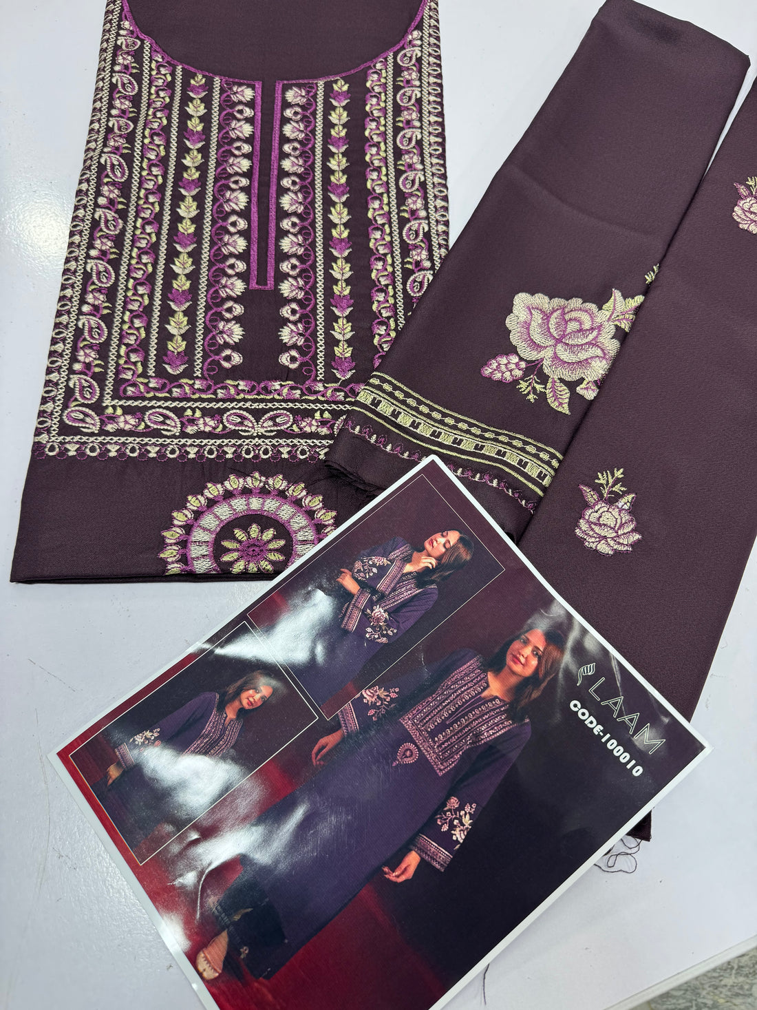 A woman modeling a deep purple long kurta with intricate white and gold embroidery on the neckline, sleeves, and center front, shown on a red studio background with two smaller inset views and the LAAM brand text.
