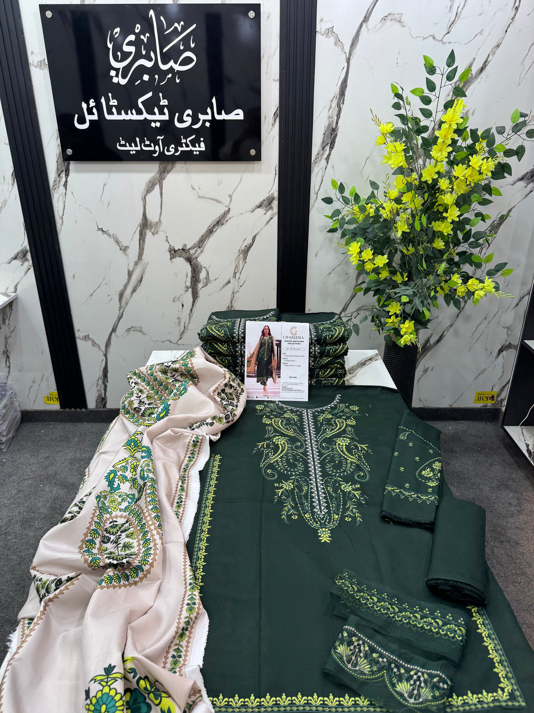 A fashion catalog page for the Charizma Winter Unstitched Collection, showing a model wearing a 3-piece ensemble consisting of a dark green embroidered Dhanak shirt, a beige printed dupatta, and a matching green and beige embroidered trouser. The right side contains product details, brand logo, and care instructions.