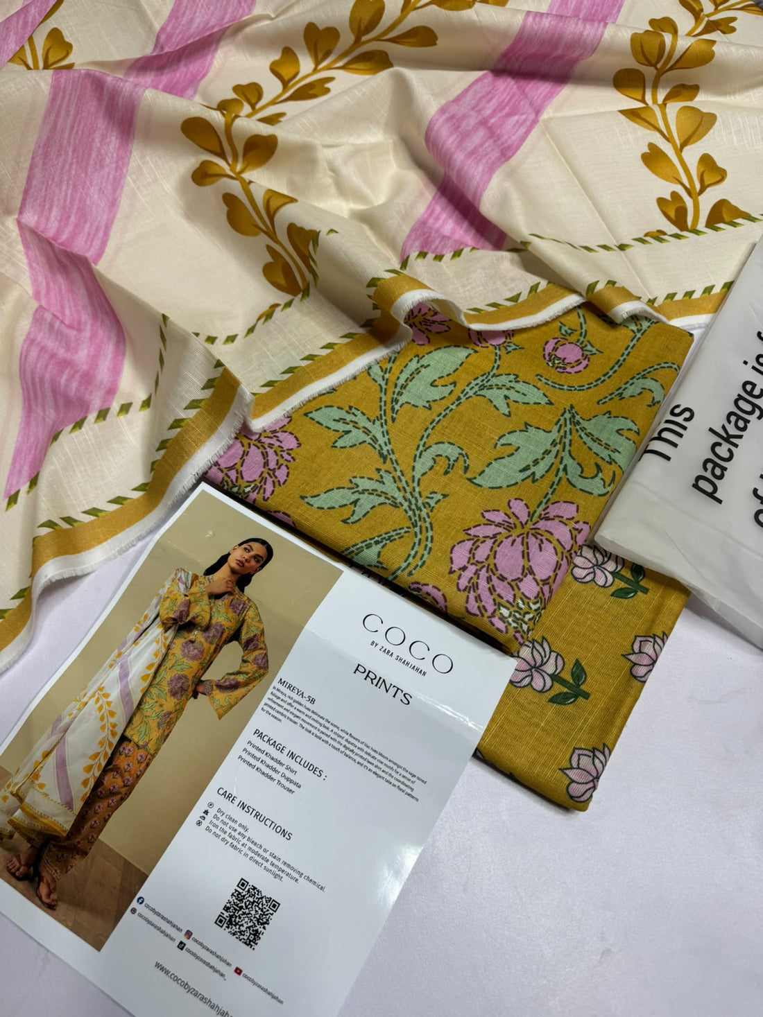 A model wearing a printed three-piece traditional outfit from ZARA SHAHJAHAN, displayed on a split background with product details, care instructions, and a QR code.