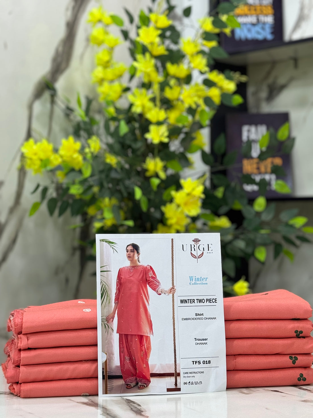 A woman modeling a coral pink embroidered Dhanak two-piece suit from the URGPEET Winter Collection, consisting of a long kurta and wide-leg trousers, standing next to a rope prop.