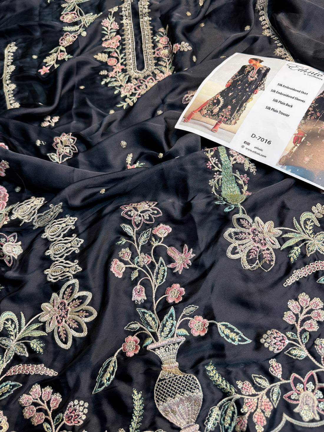 A black long-sleeve embroidered shirt dress with pink floral embroidery and gold accents, shown on a model in a studio setting with a text panel in the center listing product details.