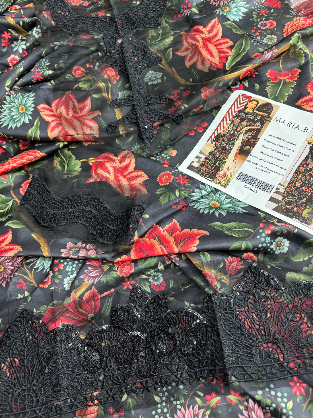 A fashion catalog-style composite showing a model wearing a black shams silk printed outfit with floral embroidery and a beige dupatta, alongside text listing features and the brand MARIA.B.