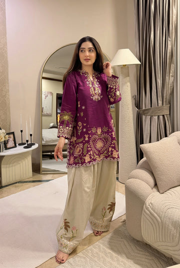 Woman in a purple embroidered outfit standing in a stylish living room.