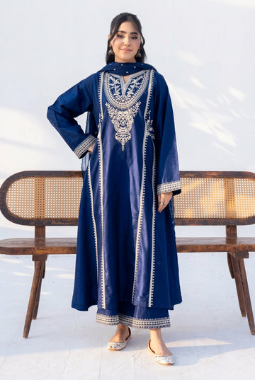A woman modeling a navy blue long kurta with intricate silver embroidery on the chest and borders, standing in front of a wooden bench against a white background.