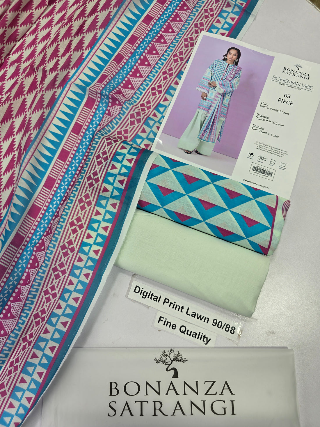 A model wearing a Bonanza Satrani 'Bohemian Vibe' unstitched collection 03-piece outfit. The set includes a multicolor geometric patterned shirt in blue, pink, and green, paired with a matching printed dupatta and light green wide-leg trousers.