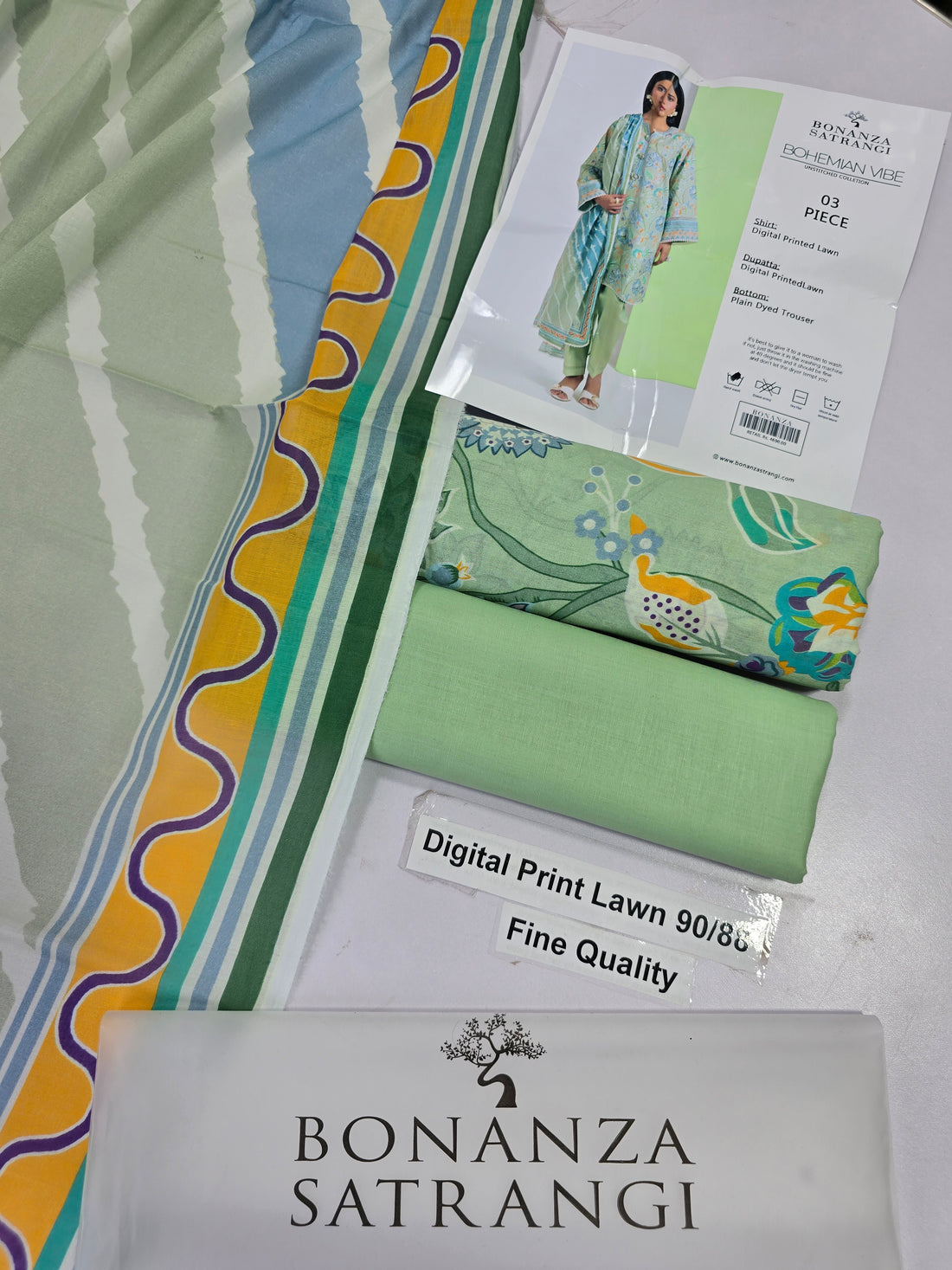 A woman modeling a three-piece unstitched outfit from Bonanza Satrani's Bohemian Vibe collection. The outfit consists of a light sage green kurta with a digital print, matching green pants, and a coordinating light green dupatta.